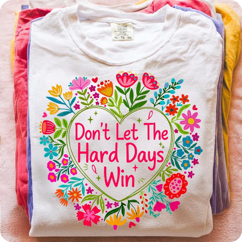Mockup of a white t-shirt featuring the 'Don't Let The Hard Days Win' sublimation graphic with a colorful boho floral heart, promoting self-love and mental health awareness.