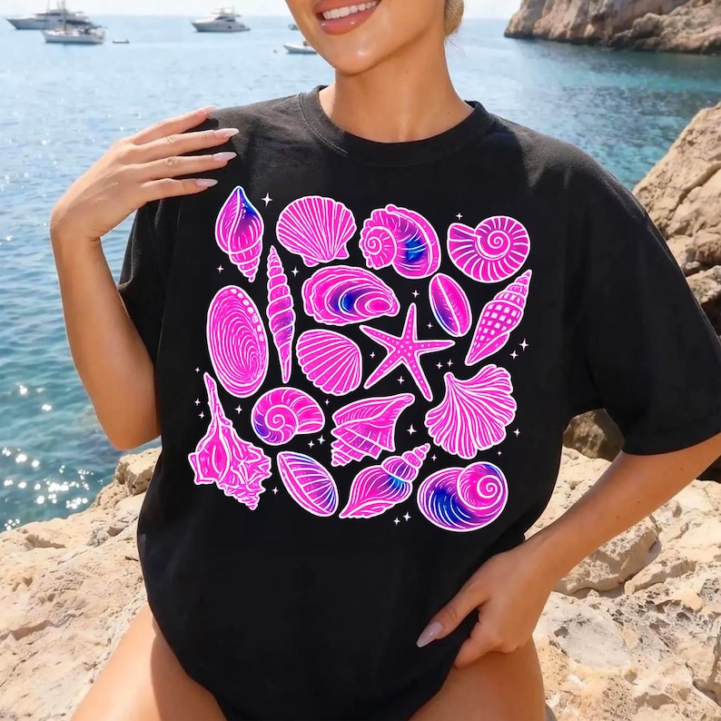 Pu&ograve; includere: T-shirt nero con un disegno di conchiglie rosa e blu. Il disegno comprende una stella marina e varie forme di conchiglie. Il disegno della maglietta &egrave; su sfondo nero.