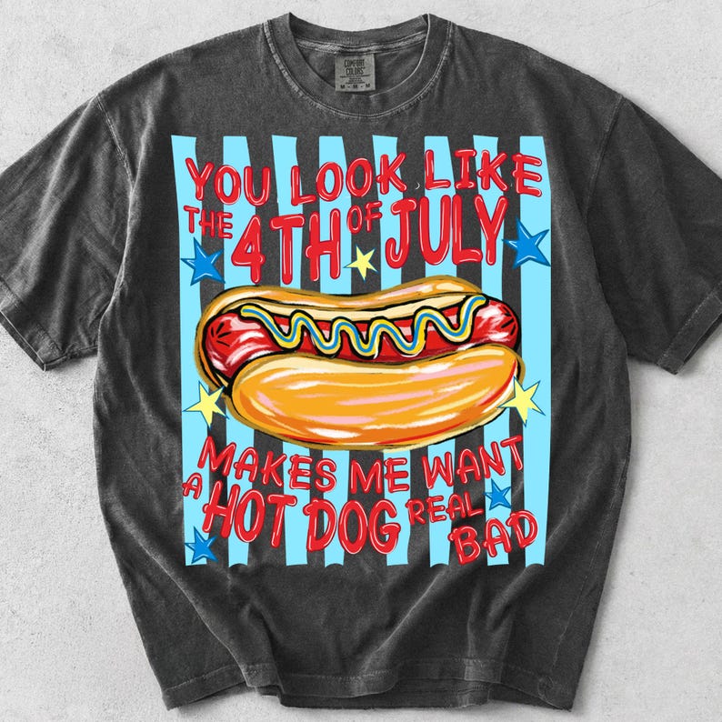 May include: Dark gray t-shirt with a graphic of a hot dog on a bun with mustard, and the text "YOU LOOK LIKE THE 4TH OF JULY MAKES ME WANT A HOT DOG REAL BAD" in red and blue.