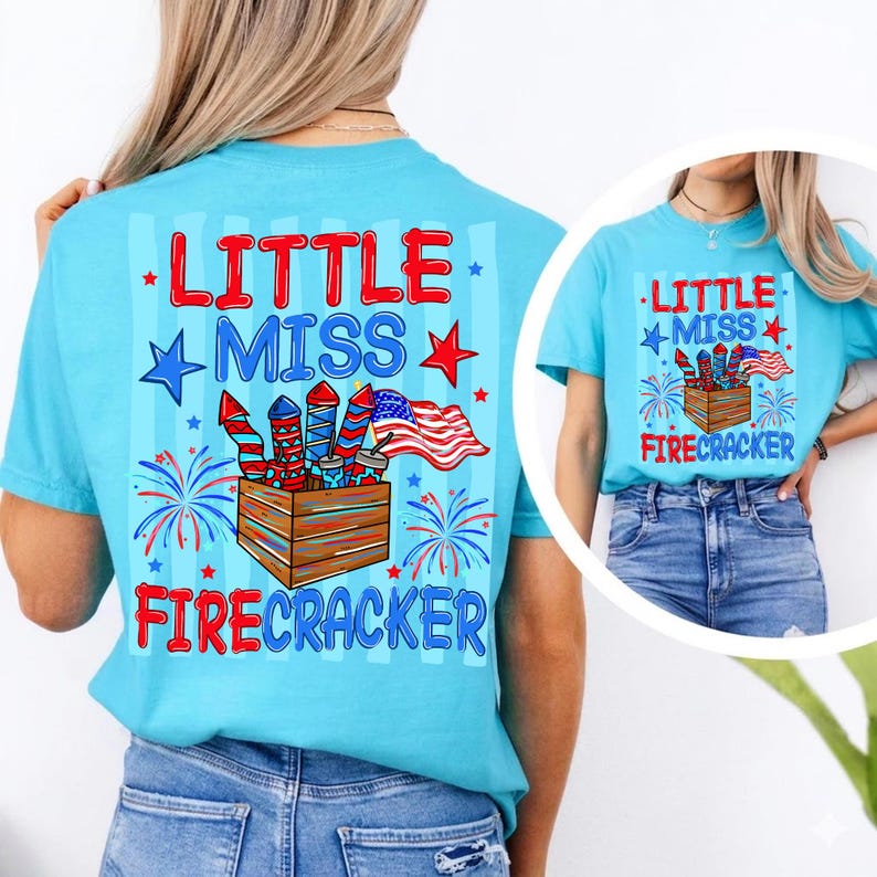 May include: A light blue t-shirt with a graphic design featuring the text "LITTLE MISS FIRECRACKER". The design includes fireworks, an American flag, and stars. The shirt is a comfortable, casual style.