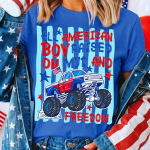 K&ouml;nnte beinhalten: Blaues T-Shirt mit einem Monster-Truck-Motiv in Rot, Wei&szlig; und Blau, mit dem Text "ALL AMERICAN BOY RAISED ON MUD AND FREEDOM". Das Design beinhaltet Sterne und Streifen.