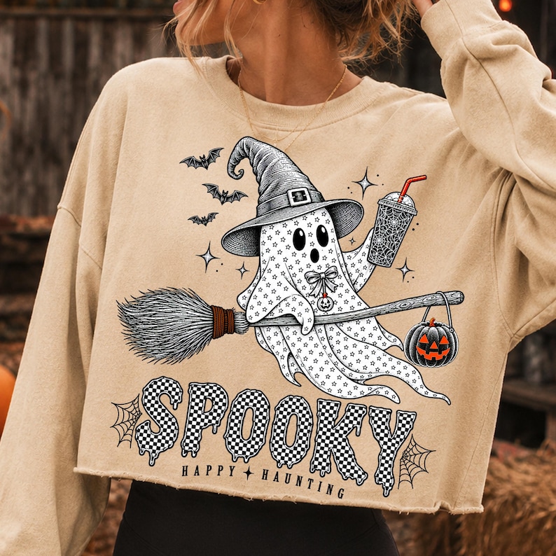 May include: A beige cropped sweatshirt featuring a graphic of a ghost wearing a witch hat, holding a drink and a broomstick with a jack-o'-lantern. The design includes bats, stars, and the text "SPOOKY HAPPY HAUNTING" in a black and white checkered pattern.