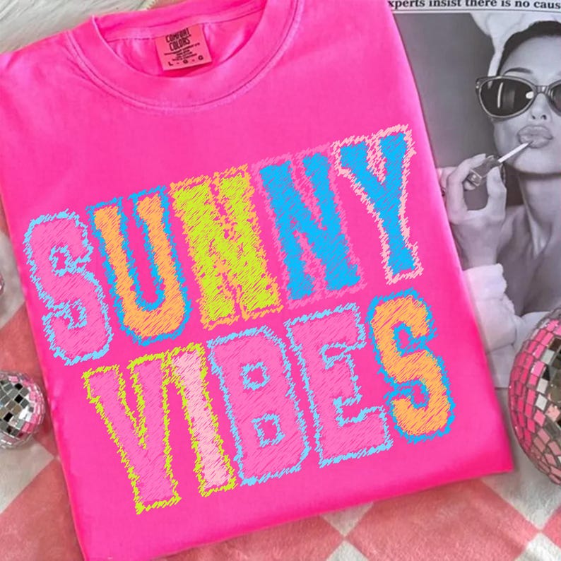 May include: Bright pink crew neck sweatshirt with the words "SUNNY VIBES" in a colorful, stitched font. The letters are outlined in blue, yellow, and orange. The sweatshirt has a Comfort Colors tag.