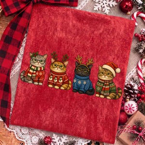 K&ouml;nnte beinhalten: Ein rotes Stoffquadrat mit einem Grafikdruck von vier Katzen, die Brillen und Weihnachtspullover tragen. Die erste Katze tr&auml;gt einen gestreiften Schal, die zweite einen Schneemann-Pullover mit Geweih, die dritte einen blauen Pullover mit Geweih.
