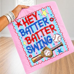 K&ouml;nnte beinhalten: Rosa Baseball-Decke mit den Worten "Hey Batter Batter Swing" in Rot und Blau. Das Design umfasst einen Baseball, einen Schl&auml;ger und einen Handschuh, mit Stern- und Blumenakzenten. Die Decke wird von einer Person gehalten.