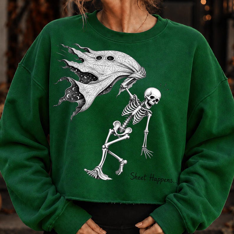 K&ouml;nnte beinhalten: Ein dunkelgr&uuml;nes Langarm-Sweatshirt mit einem wei&szlig;en Grafikdruck eines Skeletts, das ein geisterhaftes Laken mit Sternenhimmel-Muster h&auml;lt. Der Text "Sheet Happens.." ist in schwarzer Schrift unten rechts aufgedruckt.