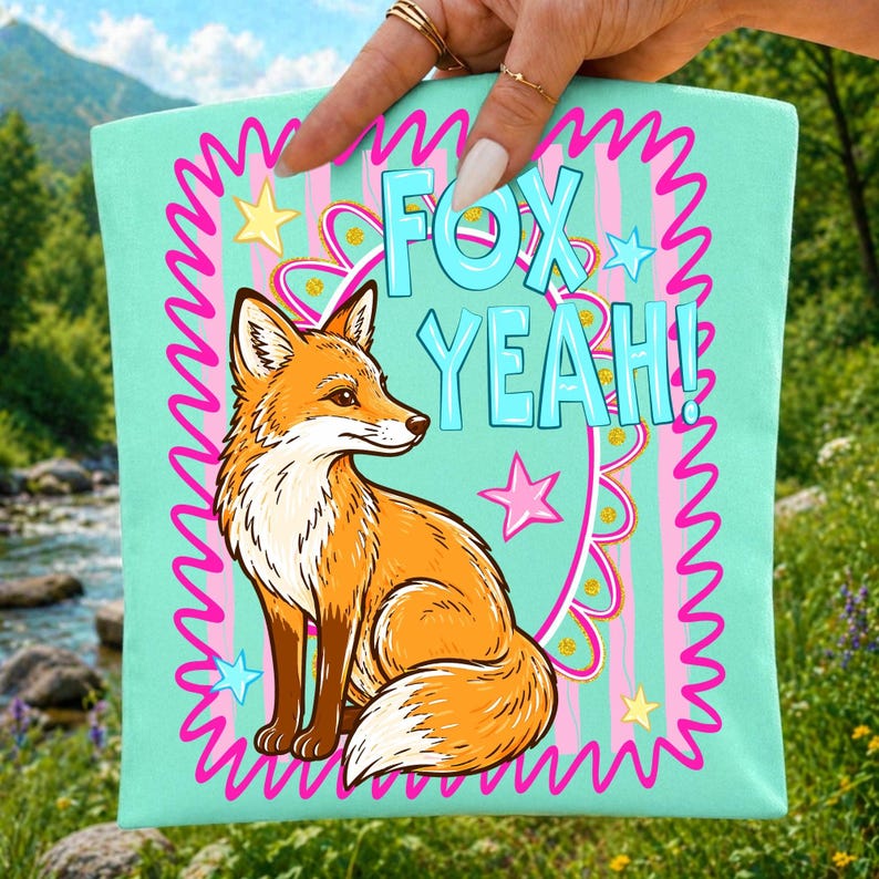 Op de afbeelding: Een turquoise draagtas met een cartoon vos illustratie. De vos is oranje en wit, met de woorden "FOX YEAH!" in blauw. Het ontwerp bevat roze sterren en een roze golvende rand. De tas wordt door een hand omhoog gehouden.