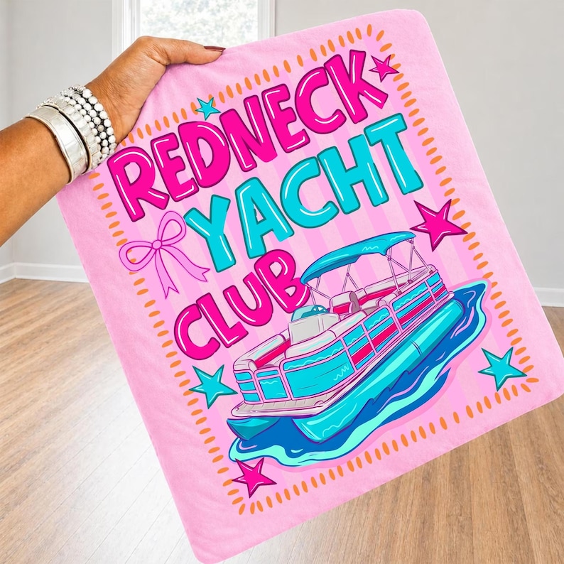 May include: Pink blanket with the words "Redneck Yacht Club" in pink and turquoise, with a cartoon boat illustration. The blanket has a pink bow and star accents.