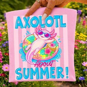 Peut inclure: Sac fourre-tout rose avec un axolotl de dessin anim&eacute; portant des lunettes de soleil et se relaxant sur une bou&eacute;e. Le texte "AXOLOTL About SUMMER!" est imprim&eacute; en bleu. Le fond a des rayures verticales.