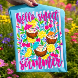 May include: A light blue t-shirt featuring a pink and white vertical striped background with the text hello sweet summer in bright pink script. The design includes illustrations of coconuts, lemon slices, cherries, ice cubes, and umbrellas.