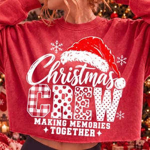 May include: A red crewneck sweatshirt featuring a white graphic print of a Santa hat above the text Christmas CREW. The word CREW is styled with plaid, polka dot, and leopard patterns. Below, the text reads MAKING MEMORIES TOGETHER.