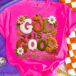 Pu&ograve; includere: Una t-shirt a maniche corte color rosa neon brillante con una grafica centrale che riporta il testo GOD IS GOOD all the time. Il design presenta lettere in stile ricamo in bianco, arancione, marrone e verde, circondate da zucche, fiori e foglie.