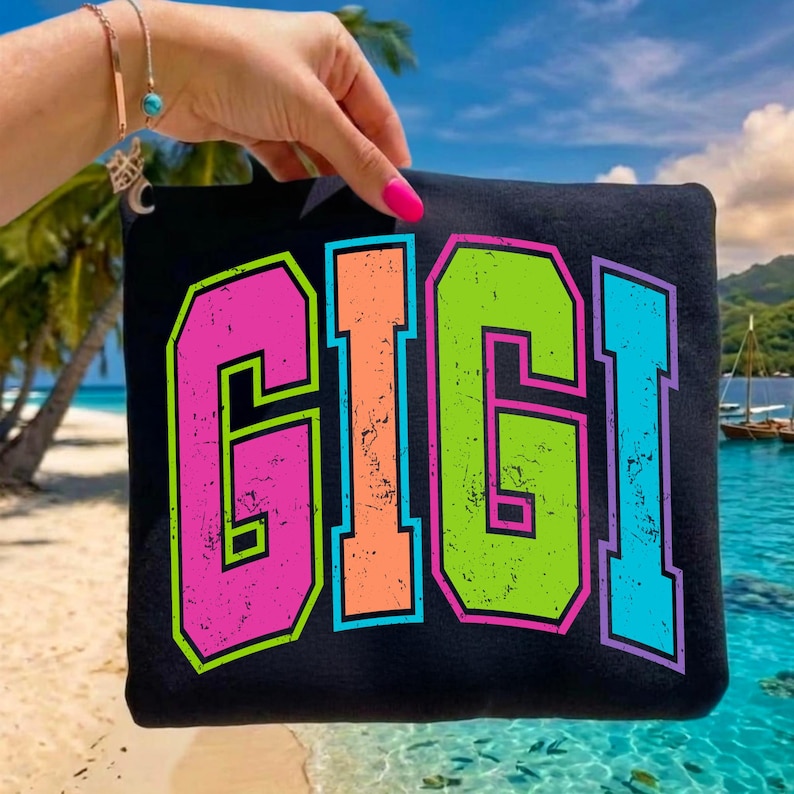 May include: Black tote bag with the name "GIGI" in large, colorful, distressed lettering. The letters are outlined in black and have a neon color scheme of pink, orange, green, and blue. The background is a tropical beach scene.