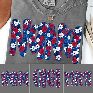May include: Gray t-shirt with the word "Nani" in large, bold letters. The letters are filled with a floral pattern in red, white, and blue. A silver necklace with a small pendant is visible. Additional images show "Gigi" and "Mimi" in the same style.