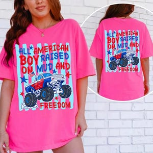 K&ouml;nnte beinhalten: Ein leuchtend pinkes T-Shirt mit dem Text "ALL AMERICAN BOY RAISED ON MUD AND FREEDOM" und einer Monster-Truck-Grafik. Das Design verwendet Rot, Wei&szlig; und Blau, mit Sternen und Streifen.