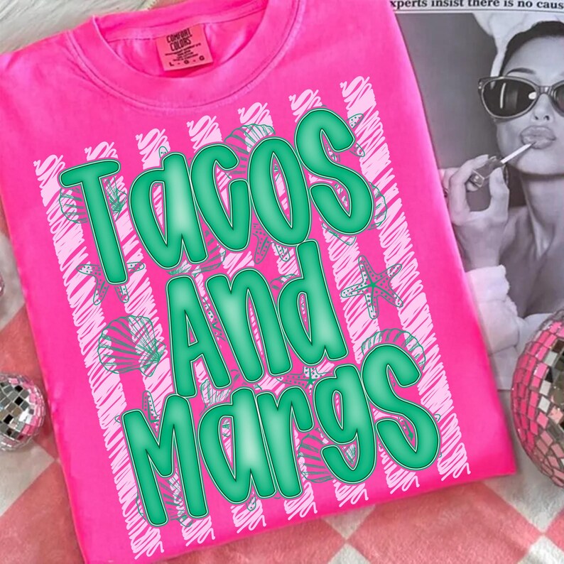 K&ouml;nnte beinhalten: Ein leuchtend pinkfarbenes T-Shirt mit dem Schriftzug "TACOS AND MARGS" in gro&szlig;en, gr&uuml;nen Buchstaben. Das Shirt hat ein gestreiftes Muster mit Seestern- und Palmenmotiven. Das Shirt ist aus einem weichen Material.