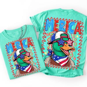 May include: Two turquoise t-shirts with a cartoon duck wearing sunglasses, a bandana, and a baseball cap. The shirts have the word "MERICA" in red and blue. The duck is green with an orange beak.