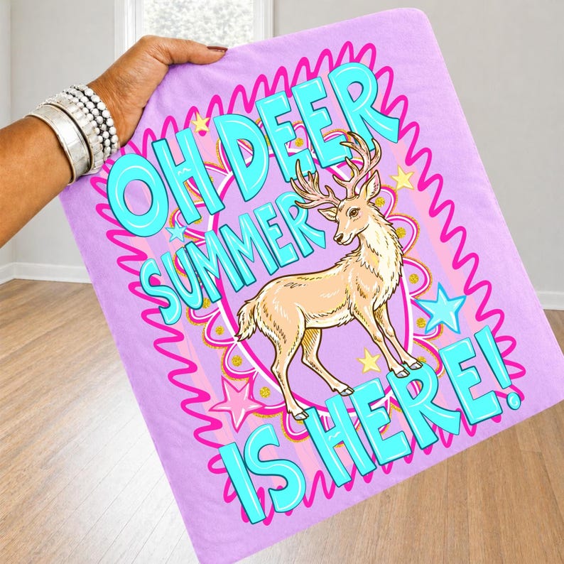 K&ouml;nnte beinhalten: Ein helllila Handtuch mit dem Text "OH DEER SUMMER IS HERE!" in T&uuml;rkis. In der Mitte befindet sich ein Cartoon-Hirsch mit Geweih. Das Design umfasst rosa Sterne und einen rosa Wellenrand.