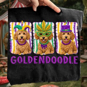 May include: Black towel featuring three Golden Doodle dog portraits, each adorned with festive Mardi Gras attire. The dogs wear a jester hat, a mask, and a top hat, with the word "GOLDENDOODLE" embroidered in purple.