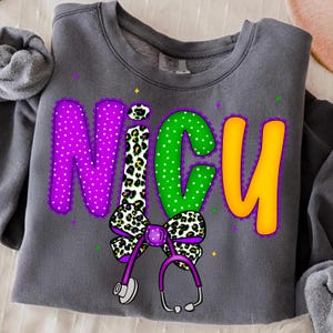 May include: Gray sweatshirt with the word "NICU" in large, colorful letters. The letters are purple with white polka dots, green with white polka dots, and yellow. A bow and stethoscope are below the letters.