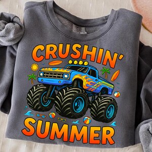 May include: Gray sweatshirt with a graphic of a blue monster truck with orange and yellow flames, the words "Crushin' Summer", a sun, palm trees, surfboards, and beach balls.
