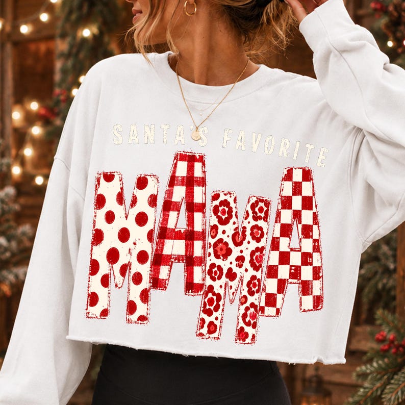 K&ouml;nnte beinhalten: Ein wei&szlig;es, lang&auml;rmeliges, bauchfreies Sweatshirt mit dem Schriftzug SANTA'S FAVORITE MAMA in roten und wei&szlig;en Mustern. Die Buchstaben MAMA sind mit roten Punkten, einem roten Karomuster, roten Blumenmustern und einem roten Schachbrettmuster gef&uuml;llt.