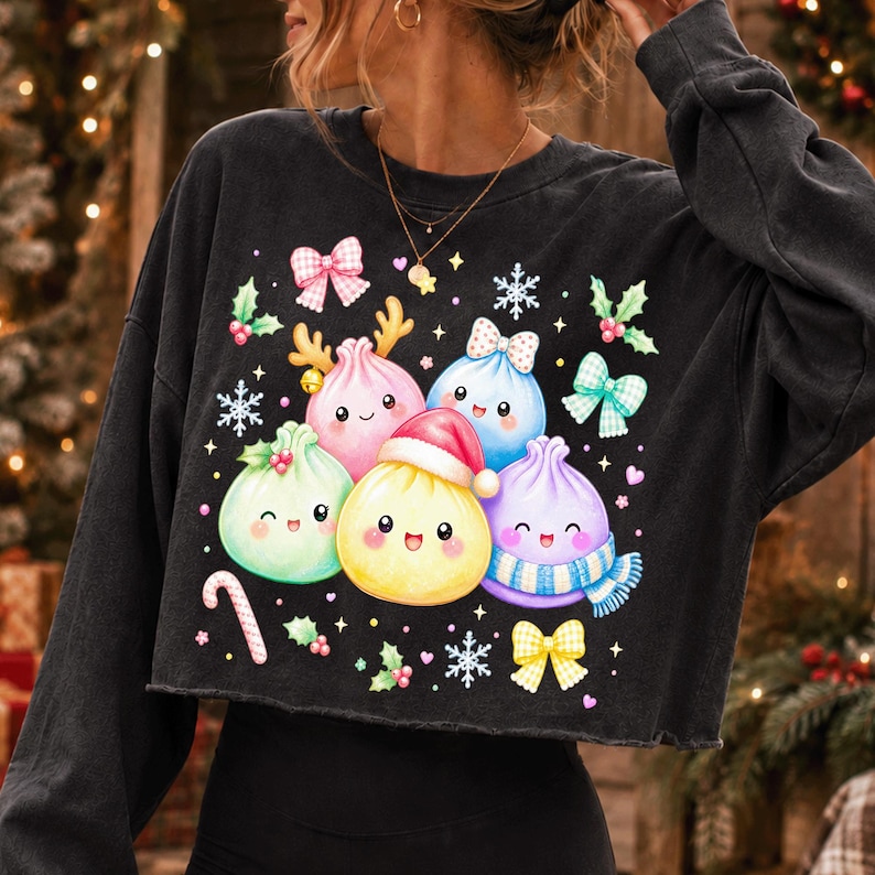 May include: A black long-sleeve cropped sweatshirt featuring a graphic print of five colourful, smiling dumpling characters. The dumplings are decorated with holiday elements including a Santa hat, reindeer antlers, a scarf, bows, holly, snowflakes, and a candy cane.