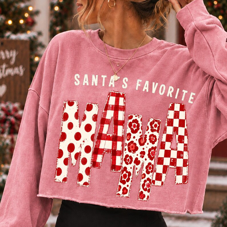 K&ouml;nnte beinhalten: Ein altrosa lang&auml;rmeliges, bauchfreies Sweatshirt mit dem wei&szlig;en Schriftzug SANTA'S FAVORITE &uuml;ber dem Wort MAMA. Die Buchstaben von MAMA sind mit verschiedenen rot-wei&szlig;en Mustern gef&uuml;llt, darunter Punkte, Vichy-Karo und Blumenmuster.