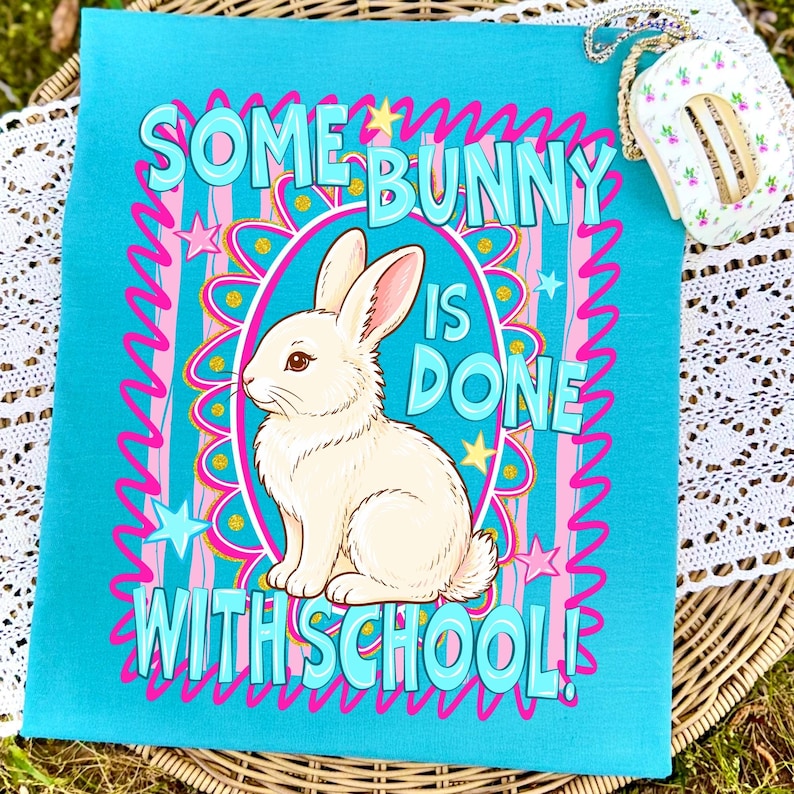Może przedstawiać: Turkusowa tkanina z napisem "SOME BUNNY IS DONE WITH SCHOOL!" w kolorze jasnoniebieskim, r&oacute;żowym i złotym. Biały kr&oacute;lik znajduje się w owalnej ramce. Projekt zawiera gwiazdy i dekoracyjne linie.