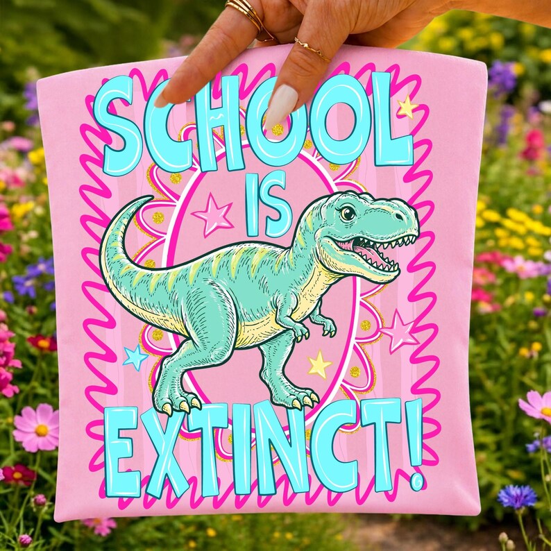 Op de afbeelding: Roze t-shirt met de tekst "SCHOOL IS EXTINCT!" in turquoise. Een cartoon Tyrannosaurus Rex in turquoise en geel staat centraal op het shirt. Het ontwerp wordt omlijst door een roze golvende rand en sterren.