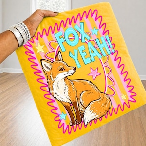 Op de afbeelding: Een gele deken met een cartoon vos illustratie. De deken heeft de woorden "FOX YEAH!" in blauw en roze. De vos is oranje en wit, en de deken heeft een roze en gele rand.