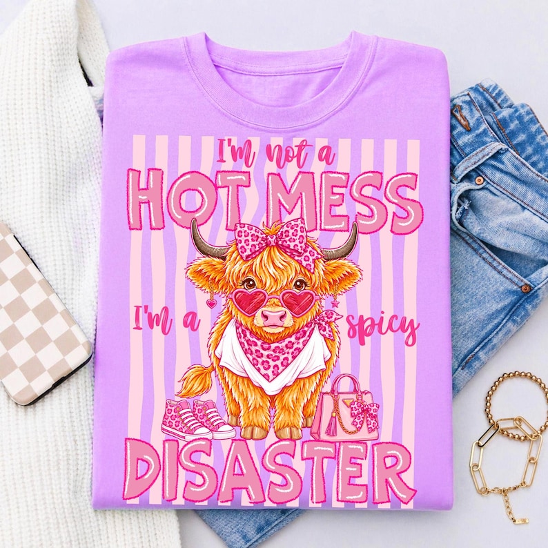 K&ouml;nnte beinhalten: Lilafarbenes T-Shirt mit einer Grafik einer Highland-Kuh mit herzf&ouml;rmiger Sonnenbrille, Schleife und Halstuch. Der Text lautet: "I'm not a HOT MESS, I'm a spicy DISASTER."