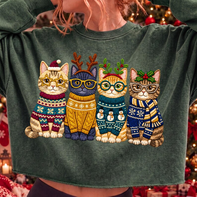 May include: A dark green long-sleeve sweatshirt featuring a graphic of four cats sitting in a row. Each cat wears glasses and a different patterned winter sweater. The cats are adorned with festive accessories including a Santa hat, reindeer antlers, holly, and a scarf.