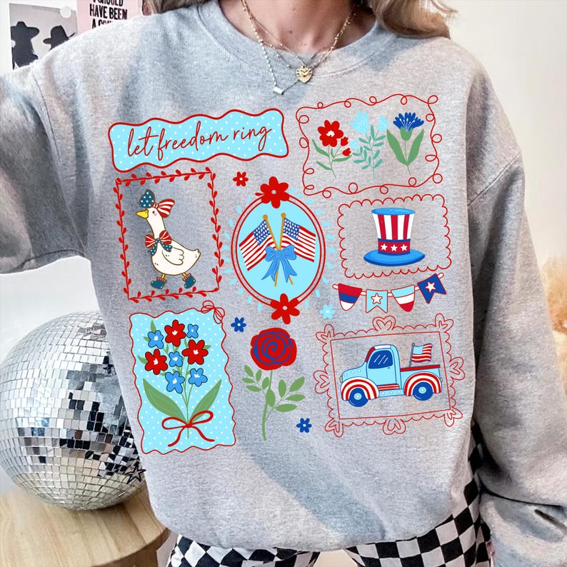 May include: A light gray sweatshirt with a patriotic design. The design includes the text "let freedom ring", a goose wearing a bow, flowers, American flags, and a truck. The graphics are in red, white, and blue.