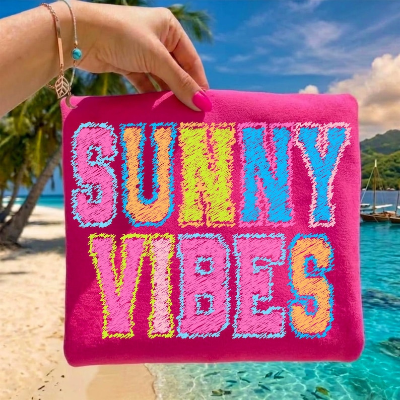 May include: A hot pink pouch with the words "SUNNY VIBES" in colorful, embroidered lettering. The pouch is held up against a tropical beach scene with palm trees, blue water, and a clear sky.