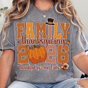 Pode incluir: Uma t-shirt cinzenta mesclada com um gr&aacute;fico que inclui o texto FAMILY thanksgiving 2026 thankful for my tribe. O design apresenta uma ab&oacute;bora laranja grande, um chap&eacute;u de peregrino castanho, bolotas, folhas de outono e um peru colorido.