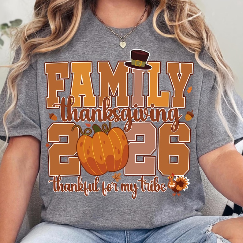 Pode incluir: Uma t-shirt cinzenta mesclada com um gr&aacute;fico que inclui o texto FAMILY thanksgiving 2026 thankful for my tribe. O design apresenta uma ab&oacute;bora laranja grande, um chap&eacute;u de peregrino castanho, bolotas, folhas de outono e um peru colorido.
