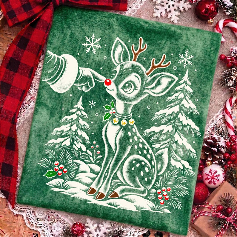 Puede incluir: Un coj&iacute;n cuadrado de terciopelo verde con una ilustraci&oacute;n blanca de un reno de nariz roja brillante siendo tocado por un dedo enguantado. El dise&ntilde;o incluye pinos nevados, copos de nieve, bayas de acebo y un collar con peque&ntilde;as campanas.