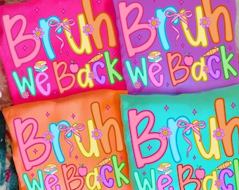 May include: Four colorful pillows with the text "Bruh We Back" in a playful font. Each pillow has a different background color: pink, purple, orange, and teal. The text is outlined in pink and features a bow, flowers, books, an apple, and a pencil.