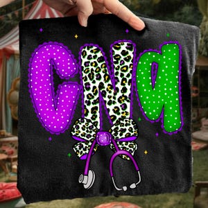 May include: Black pillow with the letters "GND" in purple, leopard print, and green. The letters are decorated with polka dots and a purple bow with a stethoscope. The design includes small star accents.