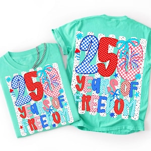 K&ouml;nnte beinhalten: Zwei minzgr&uuml;ne T-Shirts mit einem Grafikdruck mit dem Text 250 YEARS OF FREEDOM. Das Design umfasst rot-blaue Karomuster und Punkte, Feuerwerksillustrationen und hellblaue Schleifen auf einem wei&szlig;en, gestreiften Hintergrund.