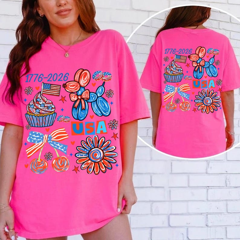 Pode incluir: Uma camiseta rosa brilhante com um design patri&oacute;tico. A frente apresenta um cupcake com uma bandeira, um cachorro de bal&atilde;o e a palavra "USA". A parte de tr&aacute;s da camisa tamb&eacute;m tem o mesmo design. O texto "1776-2026" &eacute; impresso na frente e atr&aacute;s.