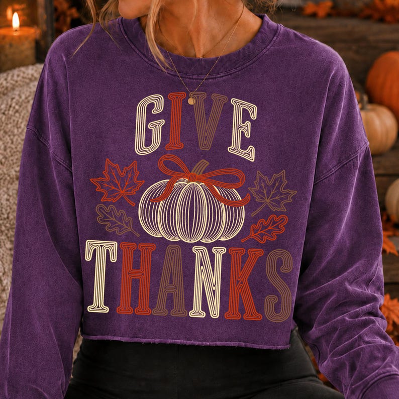 Puede incluir: Una sudadera de manga larga y cuello redondo en color morado con acabado desgastado. El frente presenta un gr&aacute;fico de una calabaza con l&iacute;neas blancas y un lazo rojo, rodeada de hojas de oto&ntilde;o y el texto GIVE THANKS en una fuente multicolor superpuesta.