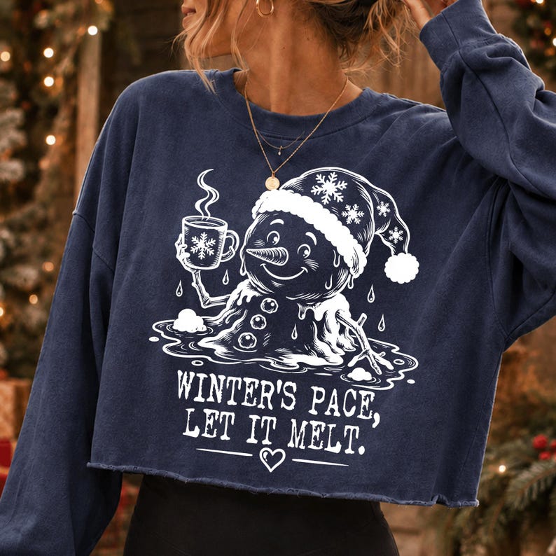 May include: A navy blue long-sleeve cropped sweatshirt featuring a white graphic of a melting snowman wearing a Santa hat and holding a steaming mug. The text reads, "WINTER'S PACE, LET IT MELT." with a small heart icon below the lettering.