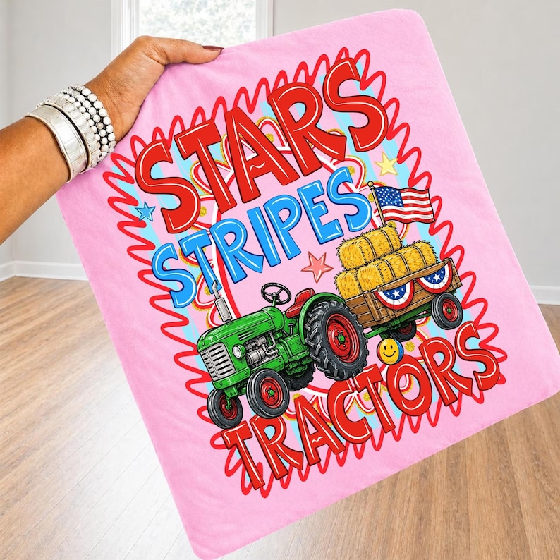 Pode incluir: Cobertor rosa com um trator verde, fardos de feno e uma bandeira americana. O cobertor tem as palavras "Stars Stripes Tractors" em vermelho e azul. O cobertor &eacute; segurado por uma pessoa.