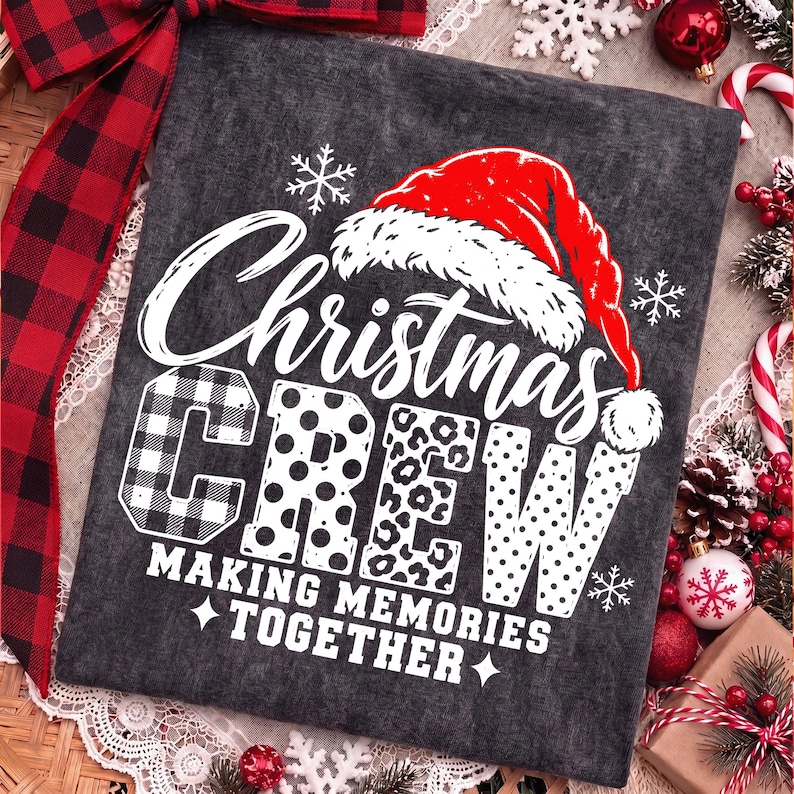 May include: A dark gray t-shirt featuring a white graphic with the text "Christmas CREW" and "MAKING MEMORIES TOGETHER". The design includes a red Santa hat, white snowflakes, and letters filled with buffalo plaid, polka dot, and leopard patterns.
