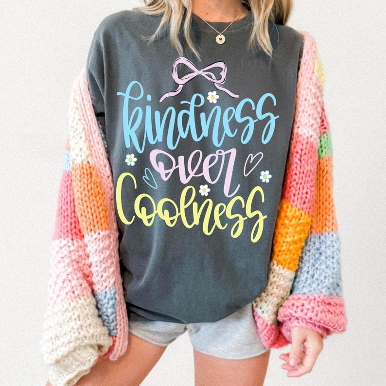 May include: Dark gray sweatshirt with the words "kindness over coolness" in pastel colors. The sweatshirt is paired with a colorful, patchwork cardigan in shades of pink, orange, yellow, and blue.