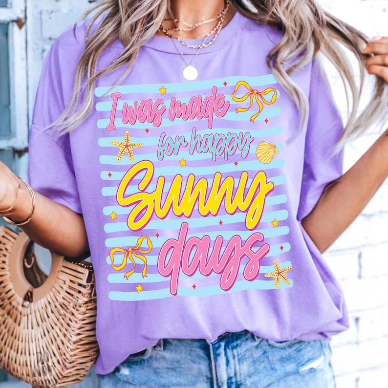 Pu&ograve; includere: T-shirt lilla con la scritta "I was made for happy sunny days" in rosa e giallo. Il design include stelle marine, fiocchi e una conchiglia. La maglietta ha una vestibilit&agrave; ampia.