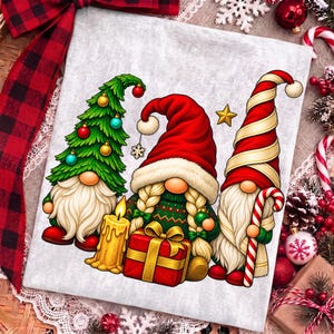 Puede incluir: Una tela gris claro con un estampado gr&aacute;fico de tres gnomos. El gnomo de la izquierda lleva un gorro de &aacute;rbol de Navidad verde con adornos. El gnomo central tiene trenzas rubias, un gorro rojo y sostiene un regalo rojo. El gnomo de la derecha lleva un gorro a rayas rojas y blancas y sostiene un bast&oacute;n de caramelo.