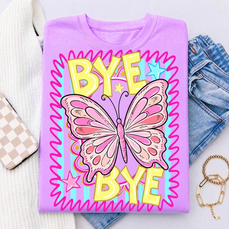 May include: A lilac t-shirt with a pink butterfly graphic and the words "BYE BYE" in yellow and pink. The design is framed by a wavy pink border, blue stars and stripes. The shirt is displayed with denim jeans and accessories.